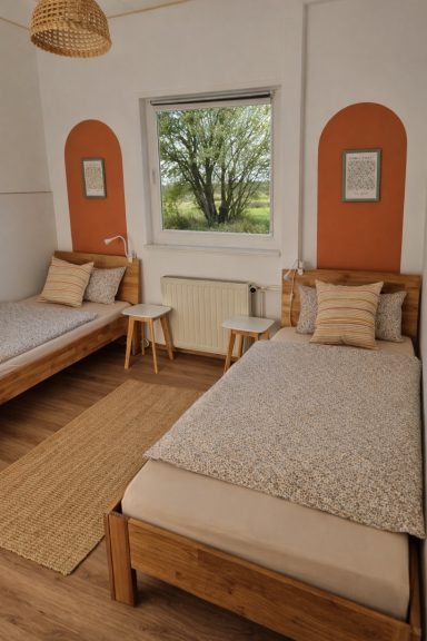 Helles Doppelzimmer mit zwei Einzelbetten, Holzmöbeln und Blick in den Garten.