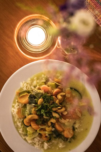 Grünes Curry mit Cashews, dekoriert mit Kerze und Blumenstrauß, House of Flow Retreat Brandenburg