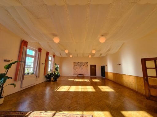 Großer, lichtdurchfluteter Seminarraum mit Parkettboden, hohen Fenstern, Pflanzen und dekorativ drapierter Stoffdecke.