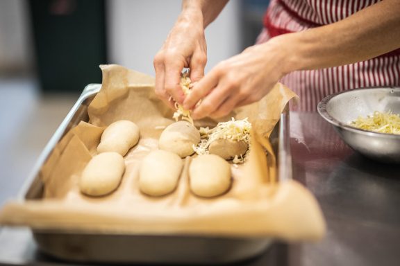 Kathrins Hände streuen Käse auf Brötchen im House of Flow, Retreat Brandenburg