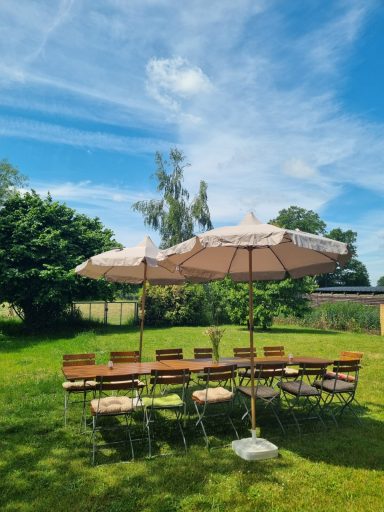 Großer Gartentisch mit Sonnenschirmen auf der Wiese des House of Flow – ideal für Pausen und Mahlzeiten im Freien.