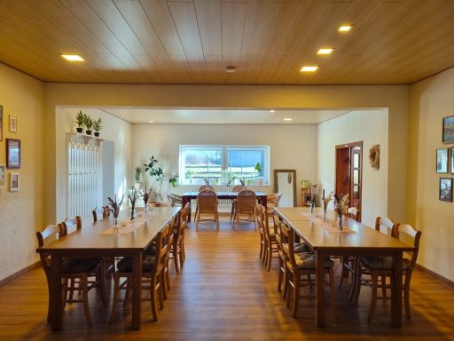 Gastraum mit großen Holztischen, Stühlen und Blick nach draußen. 