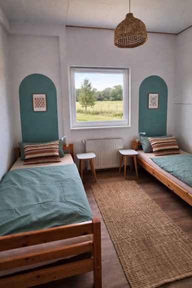 Doppelzimmer mit zwei Einzelbetten, grüner Wandgestaltung und Blick in den Garten.